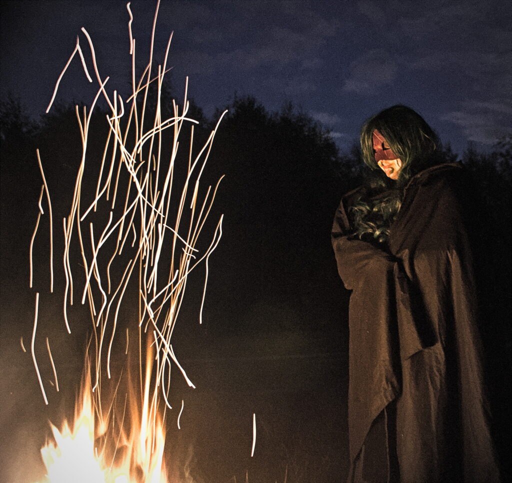 A masked woman watching the sparks of a fire rise