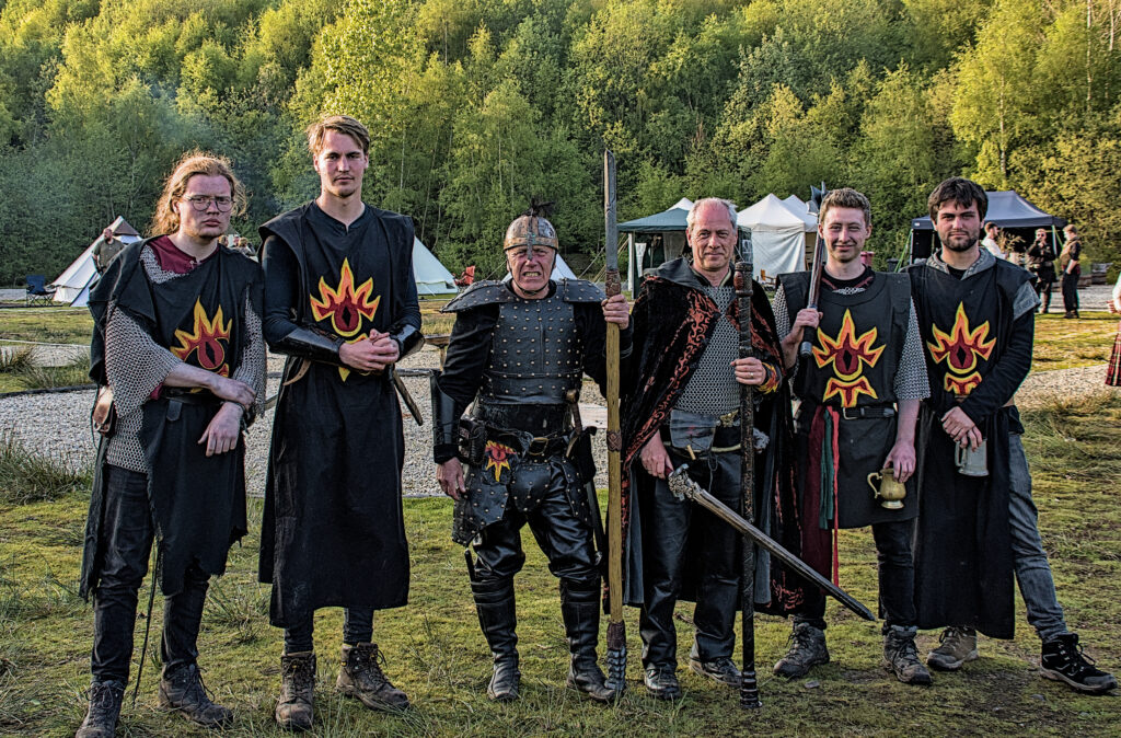 The Morgothians Herofest Group photo. 6 Men with black tabards with a stylised flaming eye symbol and armour.